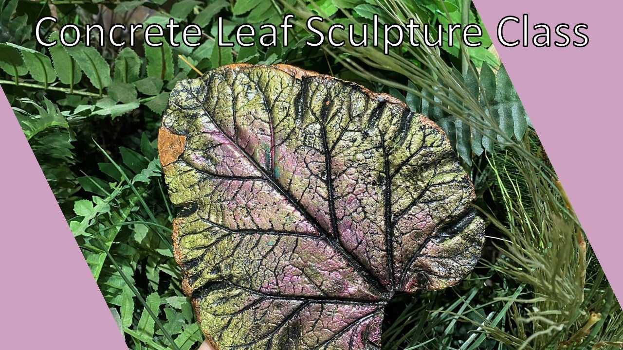 A concrete sculpture of a leaf painted green and light purple displayed in front of vibrant green plants. 