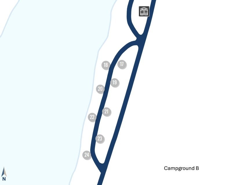 A simple map of Campground B showing a narrow loop road bordered by water on the left. Campsites numbered 17 through 24 are arranged along the loop, with 17 at the top and 24 at the bottom. A restroom icon appears near the top of the loop. A small north arrow is shown in the lower left corner, and the label "Campground B" is printed on the right side.