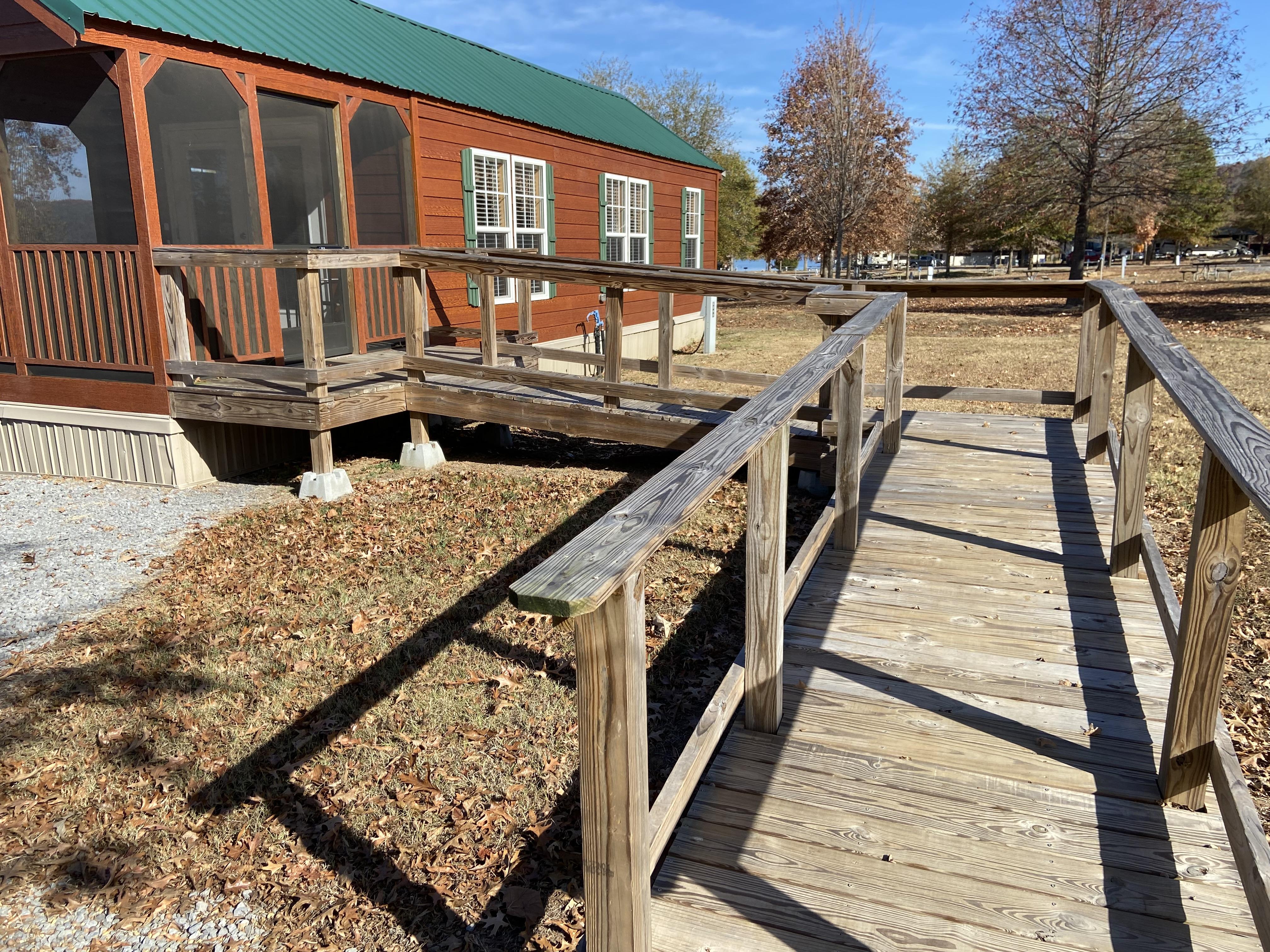 Accessible ramp leads into a wooden camper cabin with a green roof.