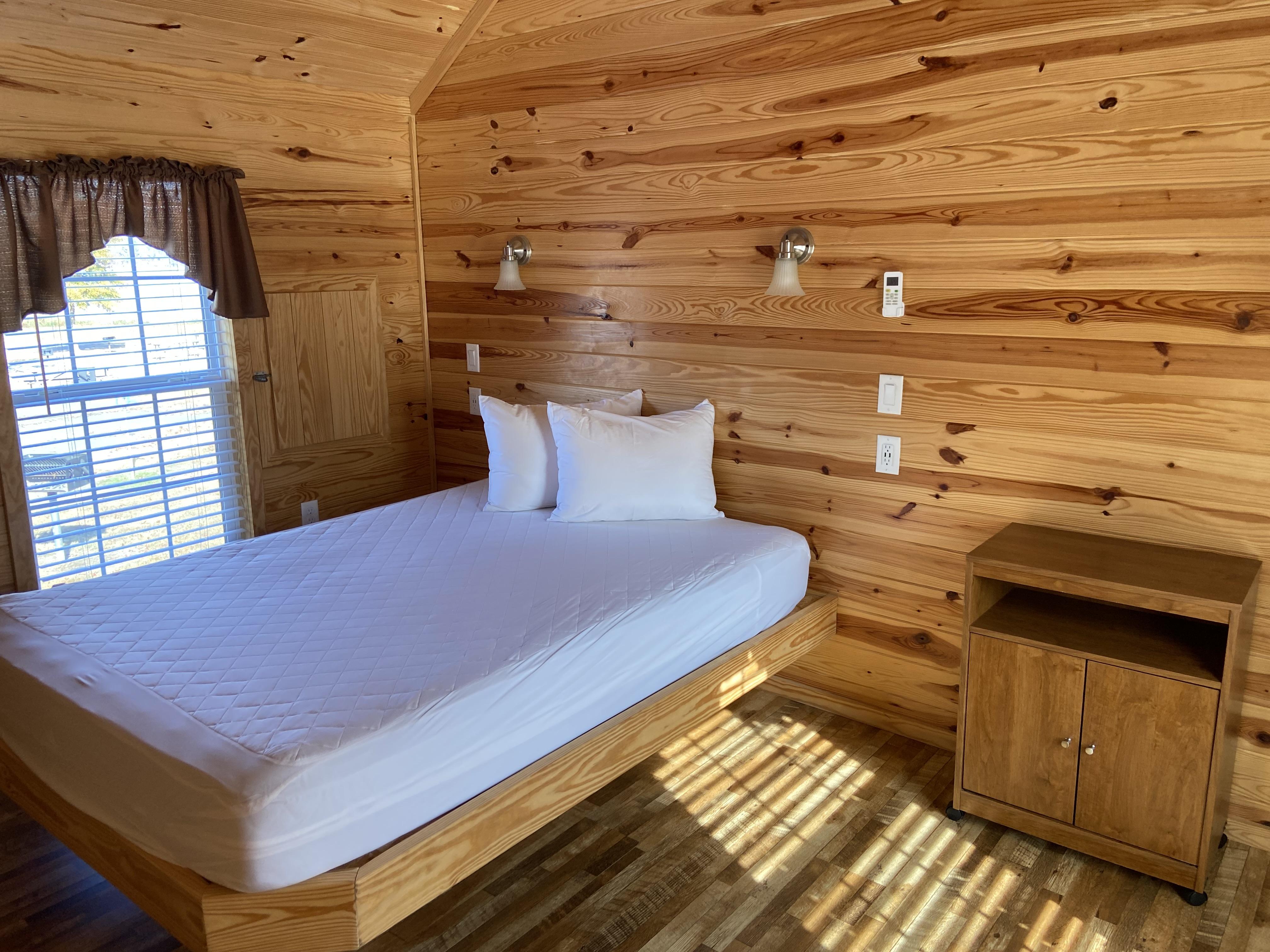 Queen bed in accessible bedroom with wooden walls, one window, and a nightstand.