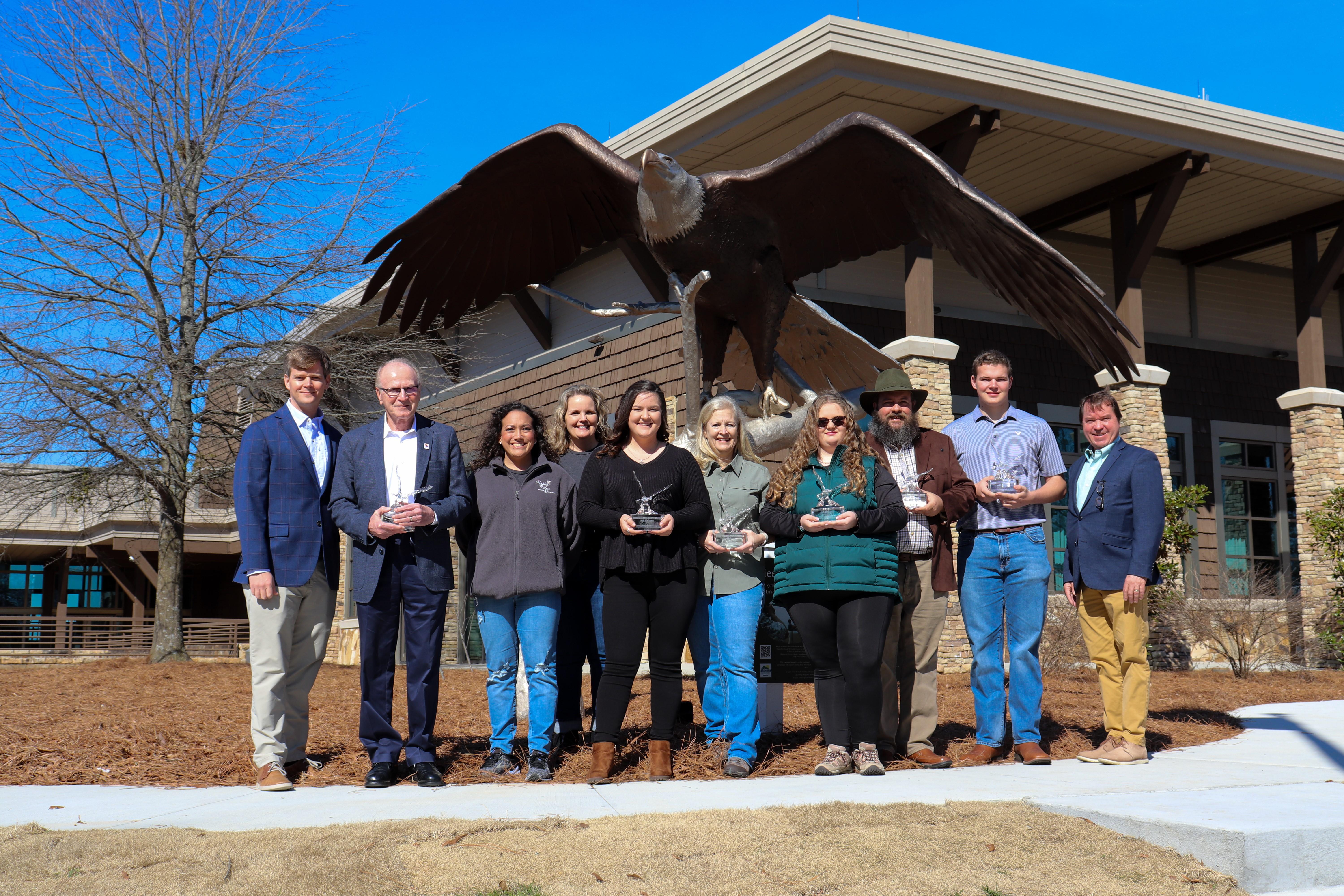 Alabama State Park Eagle Award Winners pose with trophies in front of eagle statue at Lake Guntersville State Park. The eagle statue is named Legacy.